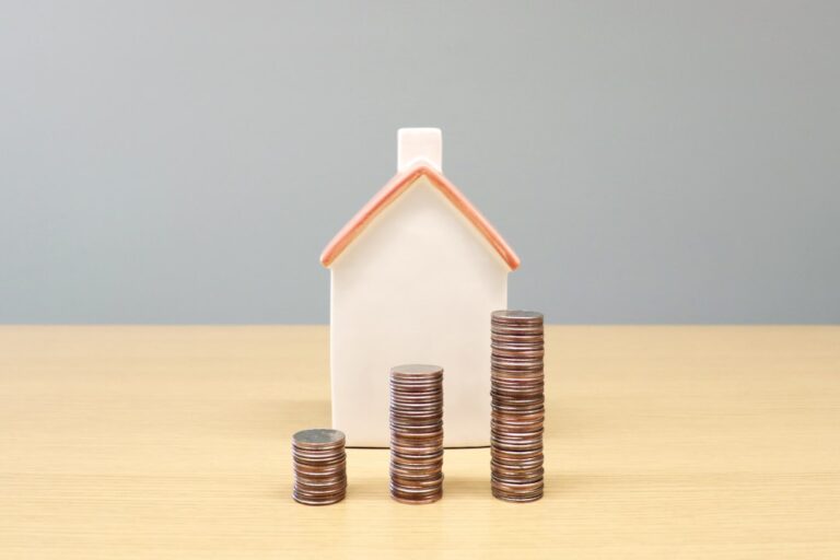Uma Casa E Pilhas De Moedas Sobre Uma Mesa UfT0GythnvE