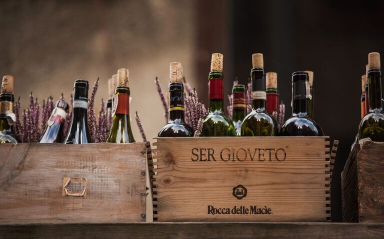Abundance of opened bottles of alcoholic beverage placed in wooden boxes on shelf against blurred background on street with blooming plant