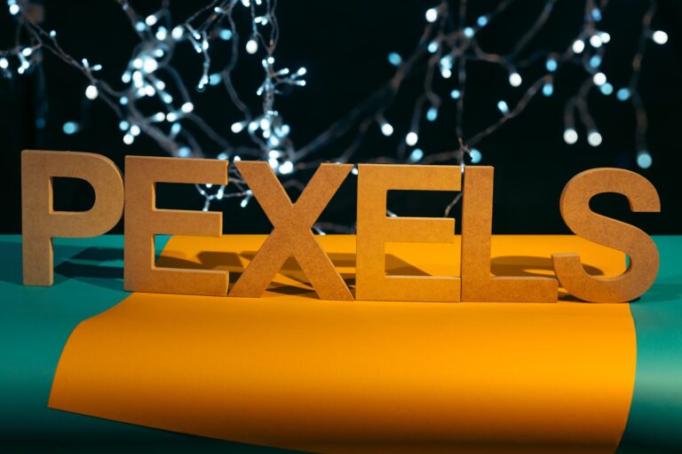 Wooden 'PEXELS' letters on a colorful backdrop with twinkling lights, perfect for creative compositions.